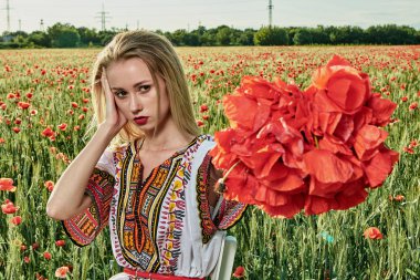 Yeşil buğday ve yabani haşhaş bir alanda beyaz kısa elbiseli uzun saçlı sarışın genç kadın.