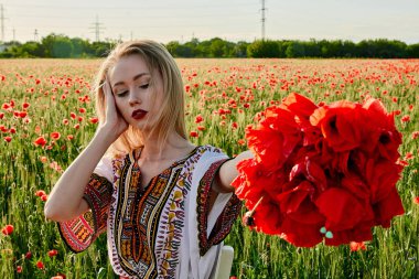 Yeşil buğday ve yabani haşhaş bir alanda beyaz kısa elbiseli uzun saçlı sarışın genç kadın.