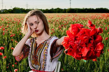 Yeşil buğday ve yabani haşhaş bir alanda beyaz kısa elbiseli uzun saçlı sarışın genç kadın.