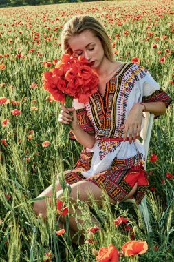 Yeşil buğday ve yabani haşhaş bir alanda beyaz kısa elbiseli uzun saçlı sarışın genç kadın.