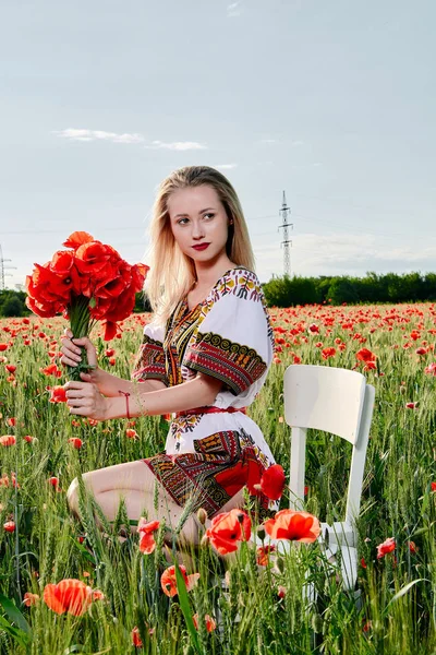 Yeşil buğday ve yabani haşhaş bir alanda beyaz kısa elbiseli uzun saçlı sarışın genç kadın.