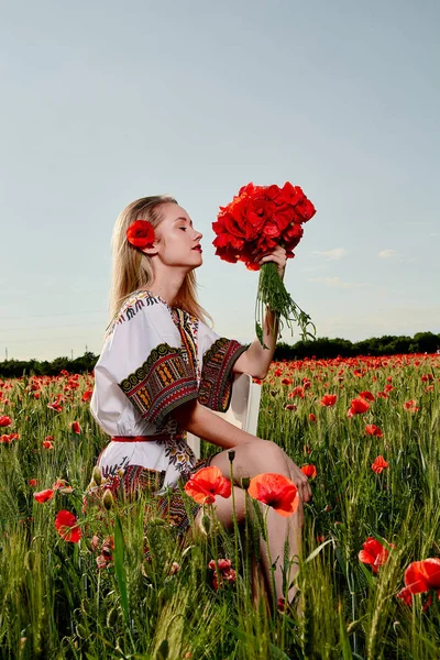 Yeşil buğday ve yabani haşhaş bir alanda beyaz kısa elbiseli uzun saçlı sarışın genç kadın.
