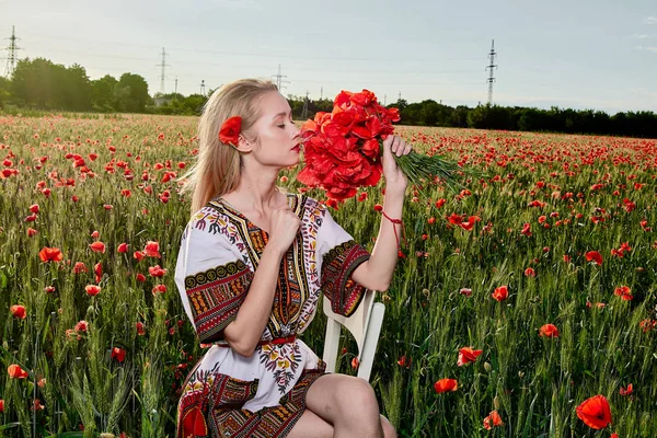 Yeşil buğday ve yabani haşhaş bir alanda beyaz kısa elbiseli uzun saçlı sarışın genç kadın.