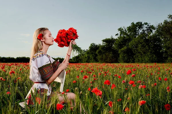 Yeşil buğday ve yabani haşhaş bir alanda beyaz kısa elbiseli uzun saçlı sarışın genç kadın.