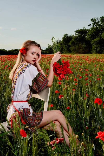 Yeşil buğday ve yabani haşhaş bir alanda beyaz kısa elbiseli uzun saçlı sarışın genç kadın.