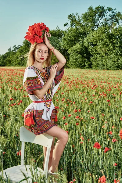 Yeşil buğday ve yabani haşhaş bir alanda beyaz kısa elbiseli uzun saçlı sarışın genç kadın.