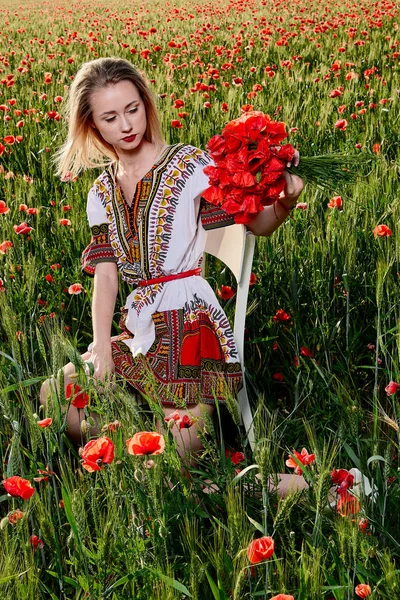 Yeşil buğday ve yabani haşhaş bir alanda beyaz kısa elbiseli uzun saçlı sarışın genç kadın.