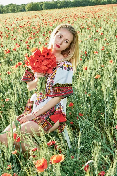 Yeşil buğday ve yabani haşhaş bir alanda beyaz kısa elbiseli uzun saçlı sarışın genç kadın.