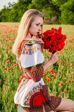 Yeşil buğday ve yabani haşhaş bir alanda beyaz kısa elbiseli uzun saçlı sarışın genç kadın.