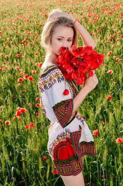 Yeşil buğday ve yabani haşhaş bir alanda beyaz kısa elbiseli uzun saçlı sarışın genç kadın.