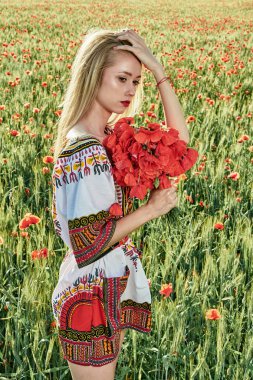 Yeşil buğday ve yabani haşhaş bir alanda beyaz kısa elbiseli uzun saçlı sarışın genç kadın.