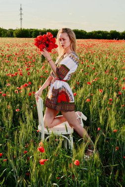 Yeşil buğday ve yabani haşhaş bir alanda beyaz kısa elbiseli uzun saçlı sarışın genç kadın.