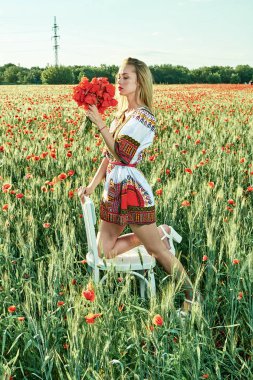 Yeşil buğday ve yabani haşhaş bir alanda beyaz kısa elbiseli uzun saçlı sarışın genç kadın.