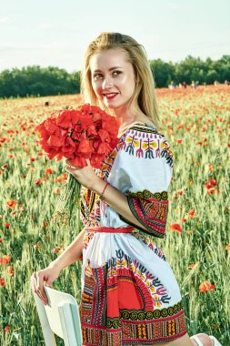 Yeşil buğday ve yabani haşhaş bir alanda beyaz kısa elbiseli uzun saçlı sarışın genç kadın.