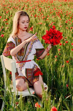 Yeşil buğday ve yabani haşhaş bir alanda beyaz kısa elbiseli uzun saçlı sarışın genç kadın.