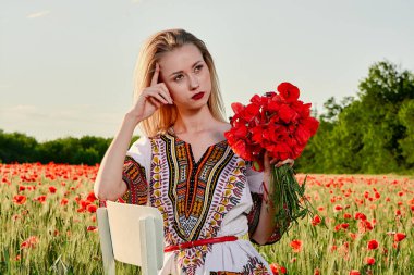 Yeşil buğday ve yabani haşhaş bir alanda beyaz kısa elbiseli uzun saçlı sarışın genç kadın.