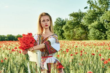 Yeşil buğday ve yabani haşhaş bir alanda beyaz kısa elbiseli uzun saçlı sarışın genç kadın.