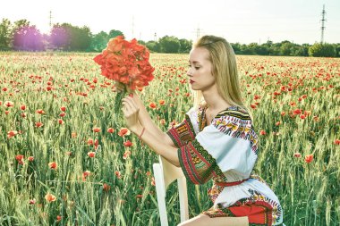 Yeşil buğday ve yabani haşhaş bir alanda beyaz kısa elbiseli uzun saçlı sarışın genç kadın.