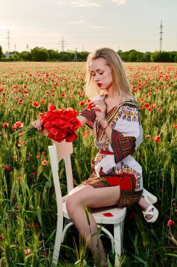 Yeşil buğday ve yabani haşhaş bir alanda beyaz kısa elbiseli uzun saçlı sarışın genç kadın.