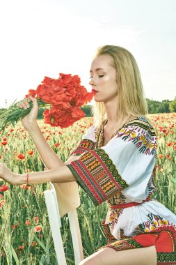 Yeşil buğday ve yabani haşhaş bir alanda beyaz kısa elbiseli uzun saçlı sarışın genç kadın.