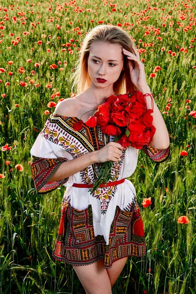 Yeşil buğday ve yabani haşhaş bir alanda beyaz kısa elbiseli uzun saçlı sarışın genç kadın.