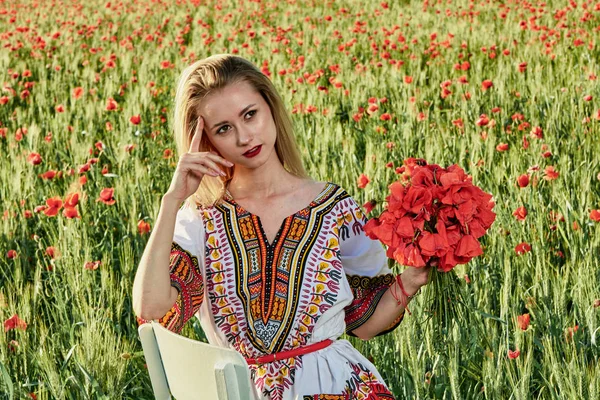 Jeune femme blonde aux cheveux longs en robe courte blanche sur un champ de blé vert et de coquelicots sauvages . — Photo