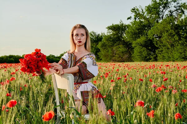Yeşil buğday ve yabani haşhaş bir alanda beyaz kısa elbiseli uzun saçlı sarışın genç kadın.
