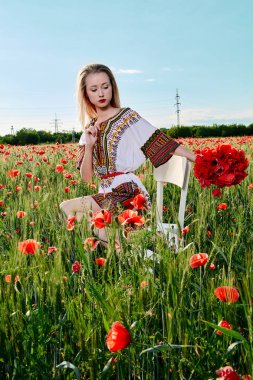 Yeşil buğday ve yabani haşhaş bir alanda beyaz kısa elbiseli uzun saçlı sarışın genç kadın.