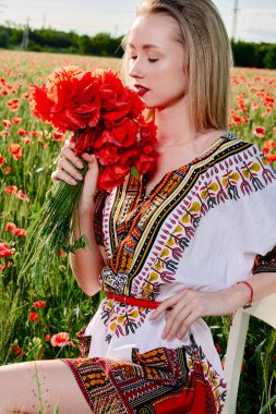 Yeşil buğday ve yabani haşhaş bir alanda beyaz kısa elbiseli uzun saçlı sarışın genç kadın.