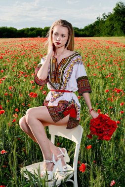 Yeşil buğday ve yabani haşhaş bir alanda beyaz kısa elbiseli uzun saçlı sarışın genç kadın.