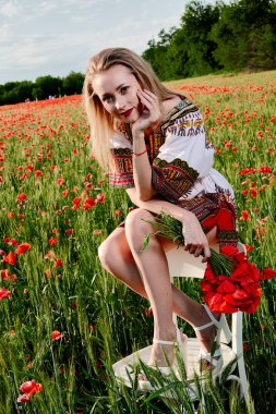 Yeşil buğday ve yabani haşhaş bir alanda beyaz kısa elbiseli uzun saçlı sarışın genç kadın.