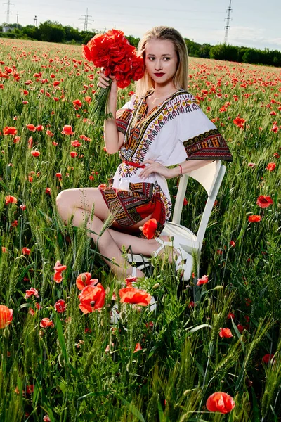 Длинноволосая блондинка в белом коротком платье на поле из зеленой пшеницы и диких маков . — стоковое фото