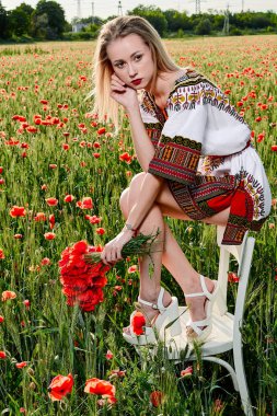 Yeşil buğday ve yabani haşhaş bir alanda beyaz kısa elbiseli uzun saçlı sarışın genç kadın.