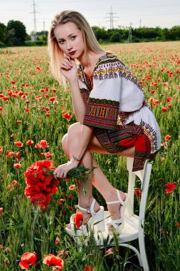 Yeşil buğday ve yabani haşhaş bir alanda beyaz kısa elbiseli uzun saçlı sarışın genç kadın.