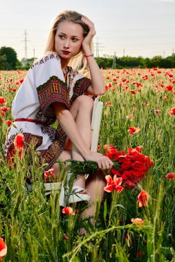 Yeşil buğday ve yabani haşhaş bir alanda beyaz kısa elbiseli uzun saçlı sarışın genç kadın.