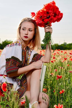 Yeşil buğday ve yabani haşhaş bir alanda beyaz kısa elbiseli uzun saçlı sarışın genç kadın.