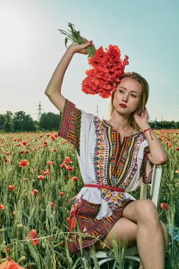 Yeşil buğday ve yabani haşhaş bir alanda beyaz kısa elbiseli uzun saçlı sarışın genç kadın.