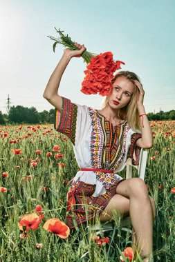 Yeşil buğday ve yabani haşhaş bir alanda beyaz kısa elbiseli uzun saçlı sarışın genç kadın.