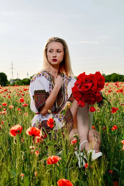 Yeşil buğday ve yabani haşhaş bir alanda beyaz kısa elbiseli uzun saçlı sarışın genç kadın.