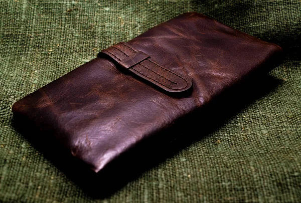 绿色粗麻布背景的旧棕色皮革钱包。特写. — 图库照片