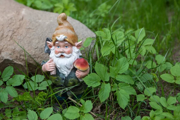 A figura de um gnomo de jardim na grama em um fundo de pedra — Fotografia de Stock