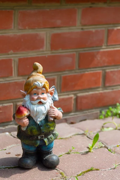 A figura de um gnomo de jardim contra uma parede de tijolo vermelho . — Fotografia de Stock