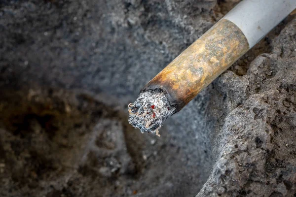 Une cigarette fumante avec des cendres sur le bord d'un cendrier en lave solidifiée. Ferme là. Espace de copie . — Photo