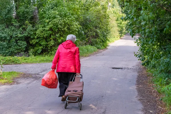 An elderly woman walking on the road. An elderly woman carries a