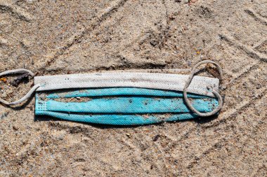 Kumlu bir yolda eski bir tıbbi maske. Yakın plan. Karantinanın sonu.