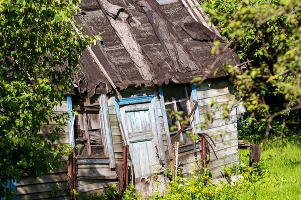 Old rickety little garden house on a sunny summer day. Blurred tree branches in the foreground.