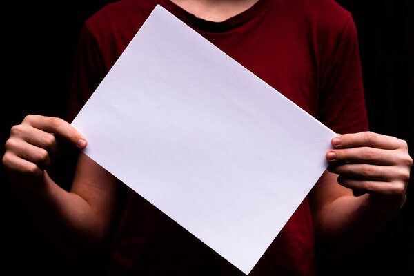 Paper sheet in the hands of a young person. Close-up. Space for lettering and design