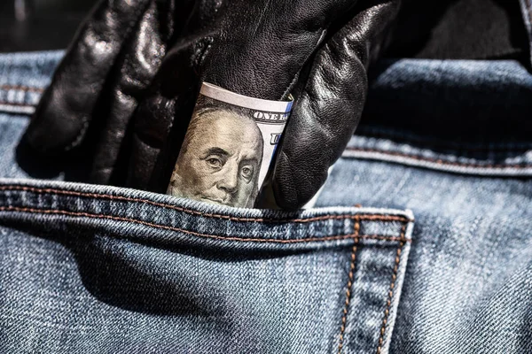 Fragment of a hundred dollar banknote. Hand in black glove pulls out a dollar bill from his pocket jeans