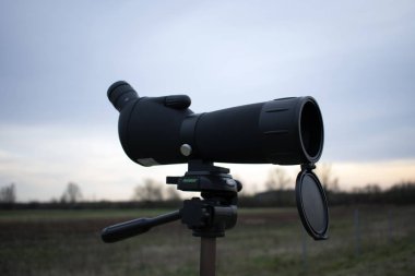 Stargazing or hunting or bird watching spotting scope on a tripod in nature. clipart