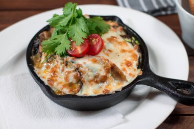 Domates, fındık, nar ve otlar ve peynir ile doldurulmuş ızgara patlıcan, siyah bir tava pişmiş. Ahşap arka plan